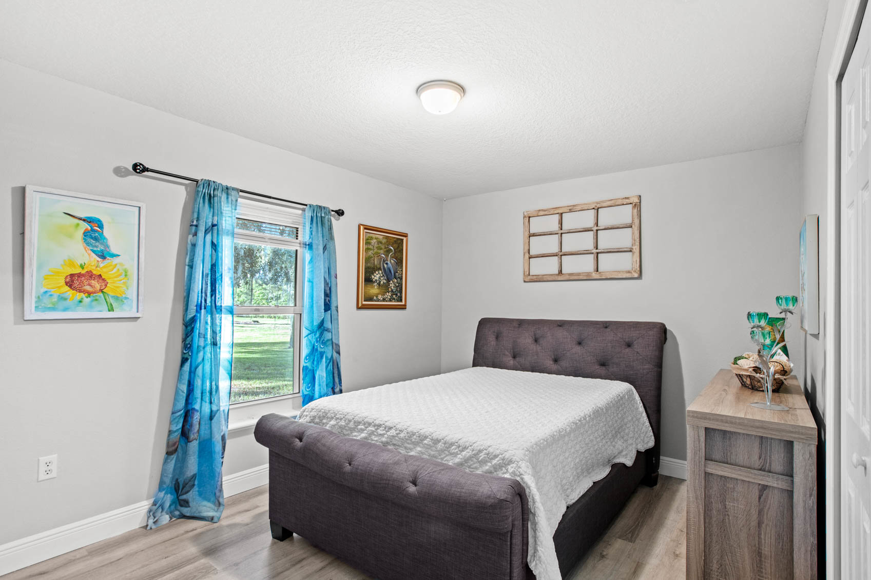 bedroom with white comforter and window with blue curtain